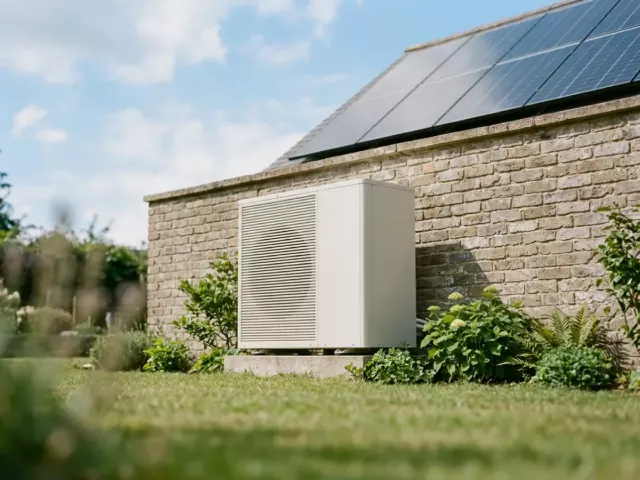 Unité extérieure de pompe à chaleur et panneaux solaires près d'une maison